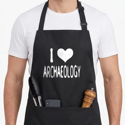 Archaeology dinosaur apron - White letter I, heart shape, and ARCHAEOLOGY text — shown on a black cotton canvas apron against a white background
