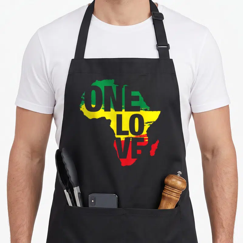 Jamaican reggae apron - ONE LOVE text over Africa map in green yellow red horizontal bands — shown on a black cotton canvas apron against a white background