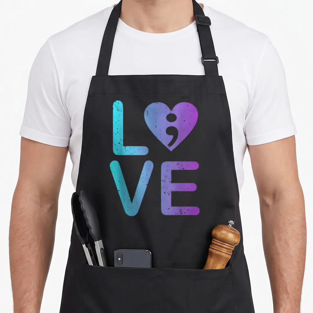 Suicide anxiety awareness apron - LOVE text in 2x2 grid with semicolon heart in cyan blue purple gradient — shown on a black cotton canvas apron against a white background