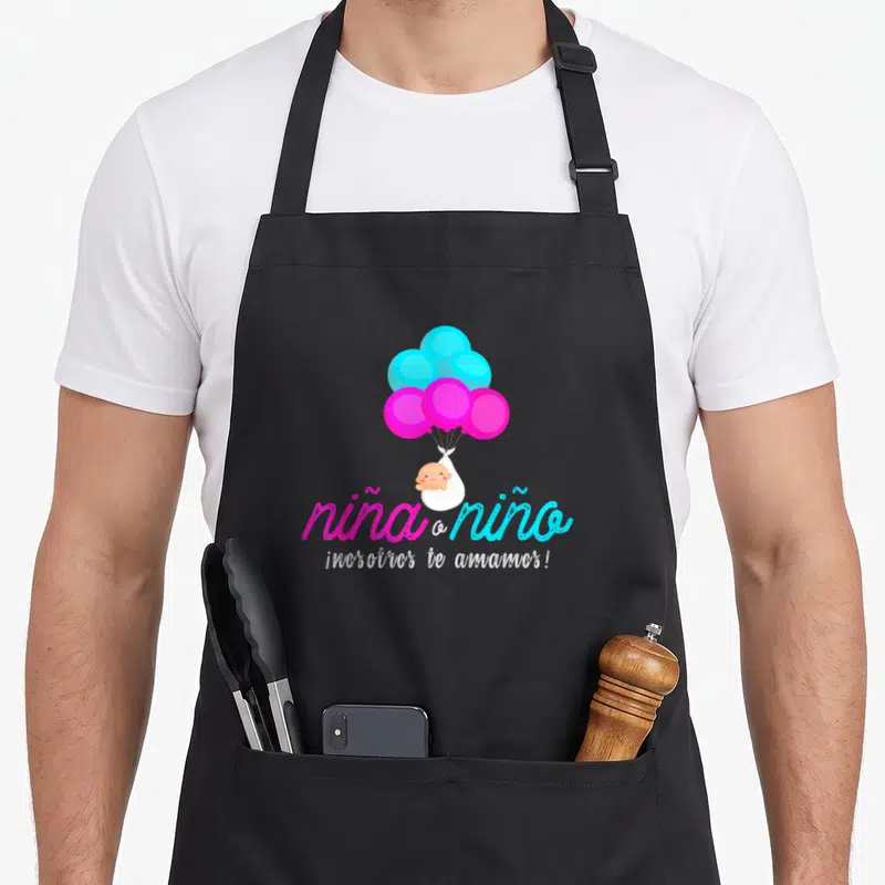 Latin apron or apron - Cartoon baby in swaddle lifted by pink and blue balloons above Spanish script — shown on a black cotton canvas apron against a white background