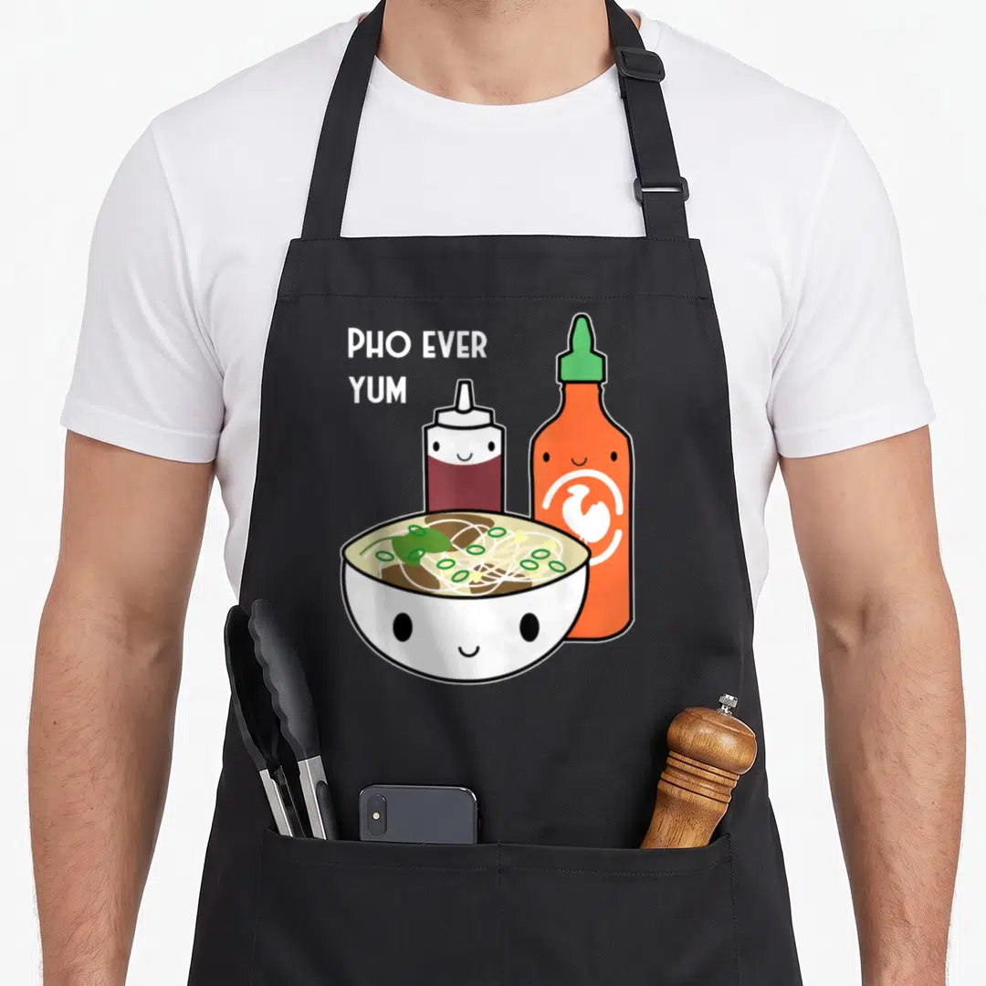 Christmas pho apron - Cartoon smiling pho bowl with hoisin and sriracha bottles and text PHO EVER YUM — shown on a black cotton canvas apron against a white background