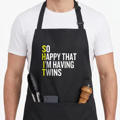 Having gemini girl apron - Stacked text with yellow vertical initials forming an acronym on white background — shown on a black cotton canvas apron against a white background