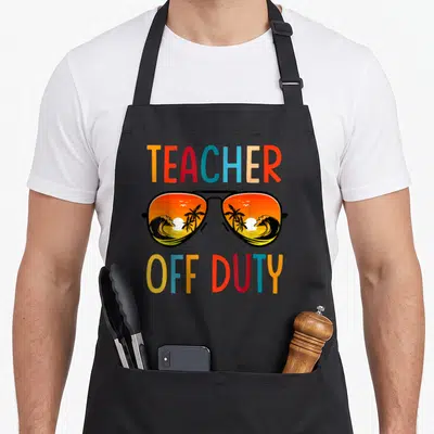 Relax spring aprons - Cartoon sunglasses with beach sunset reflection and colorful TEACHER OFF DUTY text on black fabric — shown on a black cotton canvas apron against a white background