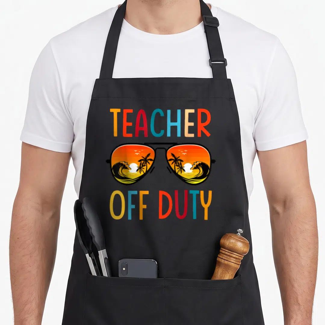 Relax spring aprons - Cartoon sunglasses with beach sunset reflection and colorful TEACHER OFF DUTY text on black fabric — shown on a black cotton canvas apron against a white background