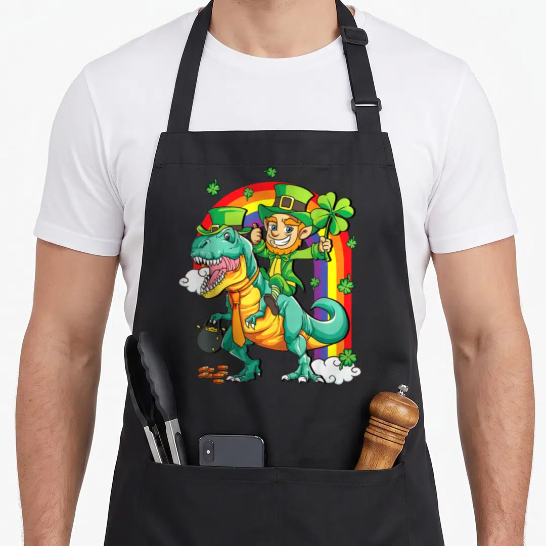 Dino toddler st patrick day aprons - Cartoon leprechaun riding teal T-Rex with pot of gold under rainbow and shamrocks — shown on a black cotton canvas apron against a white background
