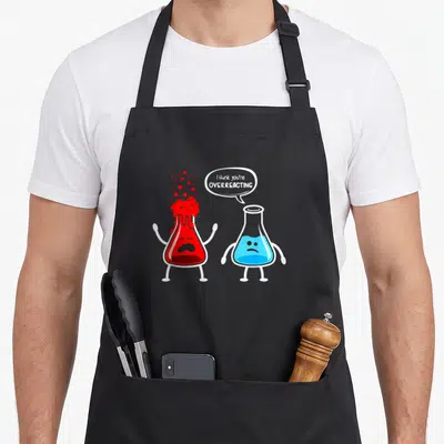 Overreacting chemistry apron - Two cartoon flasks, red bubbling and blue sad, with text I think you're overreacting — shown on a black cotton canvas apron against a white background
