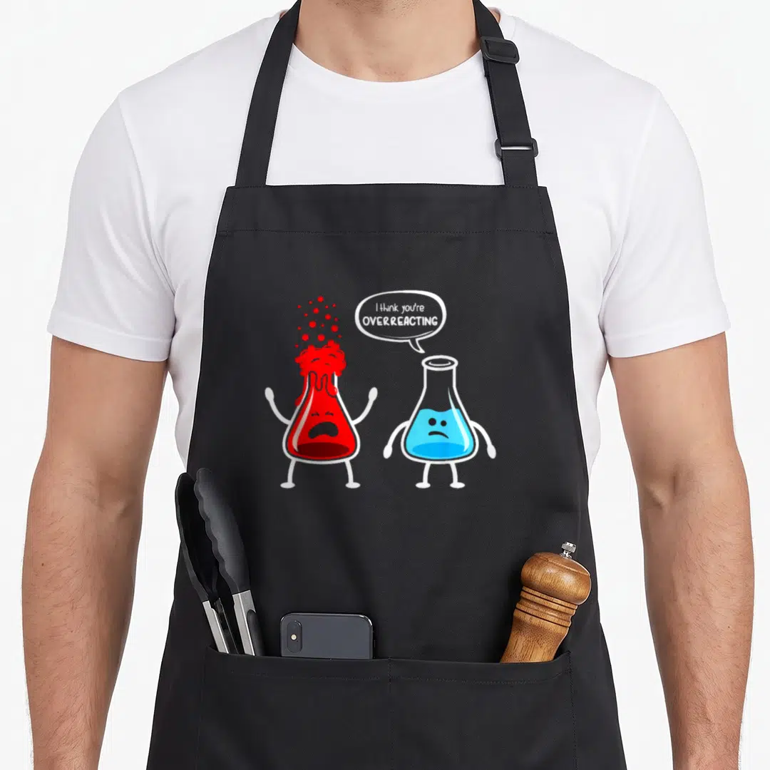 Overreacting chemistry apron - Two cartoon flasks, red bubbling and blue sad, with text I think you're overreacting — shown on a black cotton canvas apron against a white background