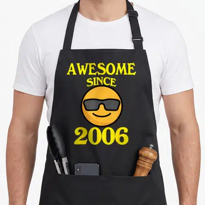 Cool 18th birthday apron - Awesome Since 2006 text surrounding a cartoon smiley face wearing grey sunglasses — shown on a black cotton canvas apron against a white background
