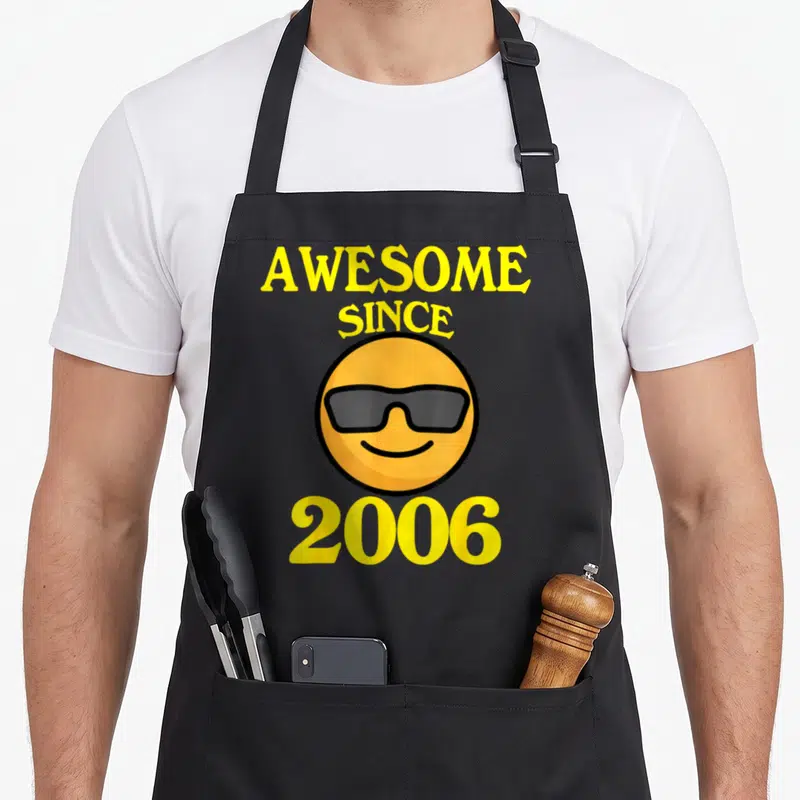Cool 18th birthday apron - Awesome Since 2006 text surrounding a cartoon smiley face wearing grey sunglasses — shown on a black cotton canvas apron against a white background