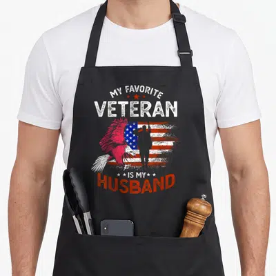 Cute veteran best husband apron - Pink eagle saluting soldier distressed flag MY FAVORITE VETERAN IS MY HUSBAND text — shown on a black cotton canvas apron against a white background