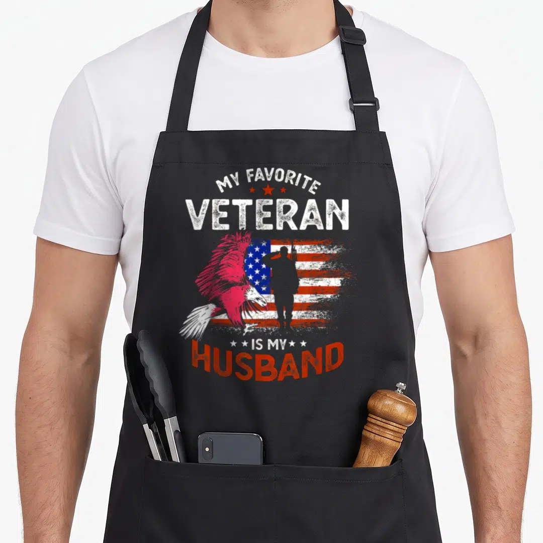 Cute veteran best husband apron - Pink eagle saluting soldier distressed flag MY FAVORITE VETERAN IS MY HUSBAND text — shown on a black cotton canvas apron against a white background