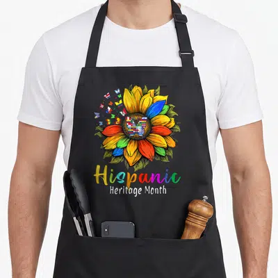 Latin sunflower apron - Multicolored sunflower with flag butterflies and Hispanic Heritage Month text — shown on a black cotton canvas apron against a white background