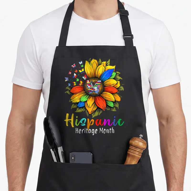 Latin sunflower apron - Multicolored sunflower with flag butterflies and Hispanic Heritage Month text — shown on a black cotton canvas apron against a white background
