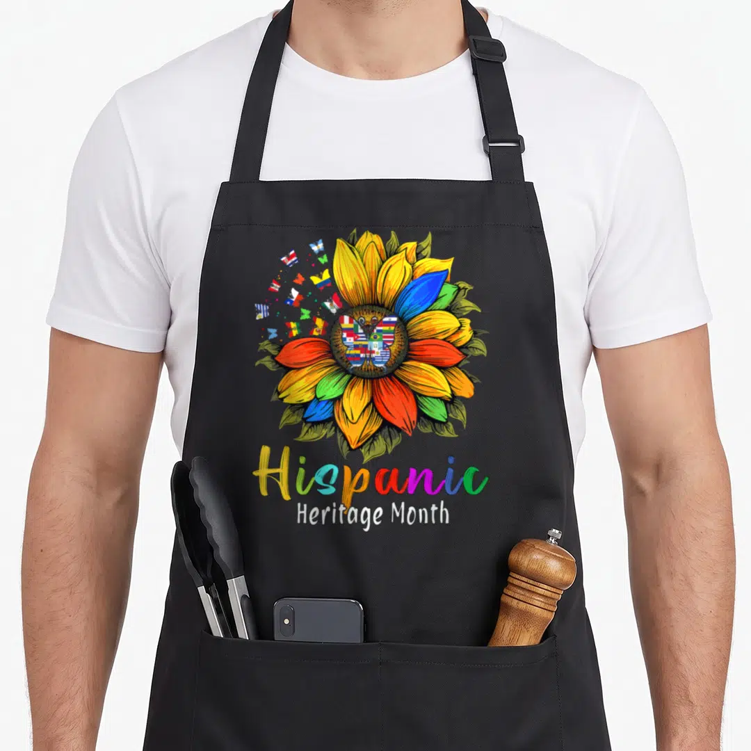 Latin sunflower apron - Multicolored sunflower with flag butterflies and Hispanic Heritage Month text — shown on a black cotton canvas apron against a white background