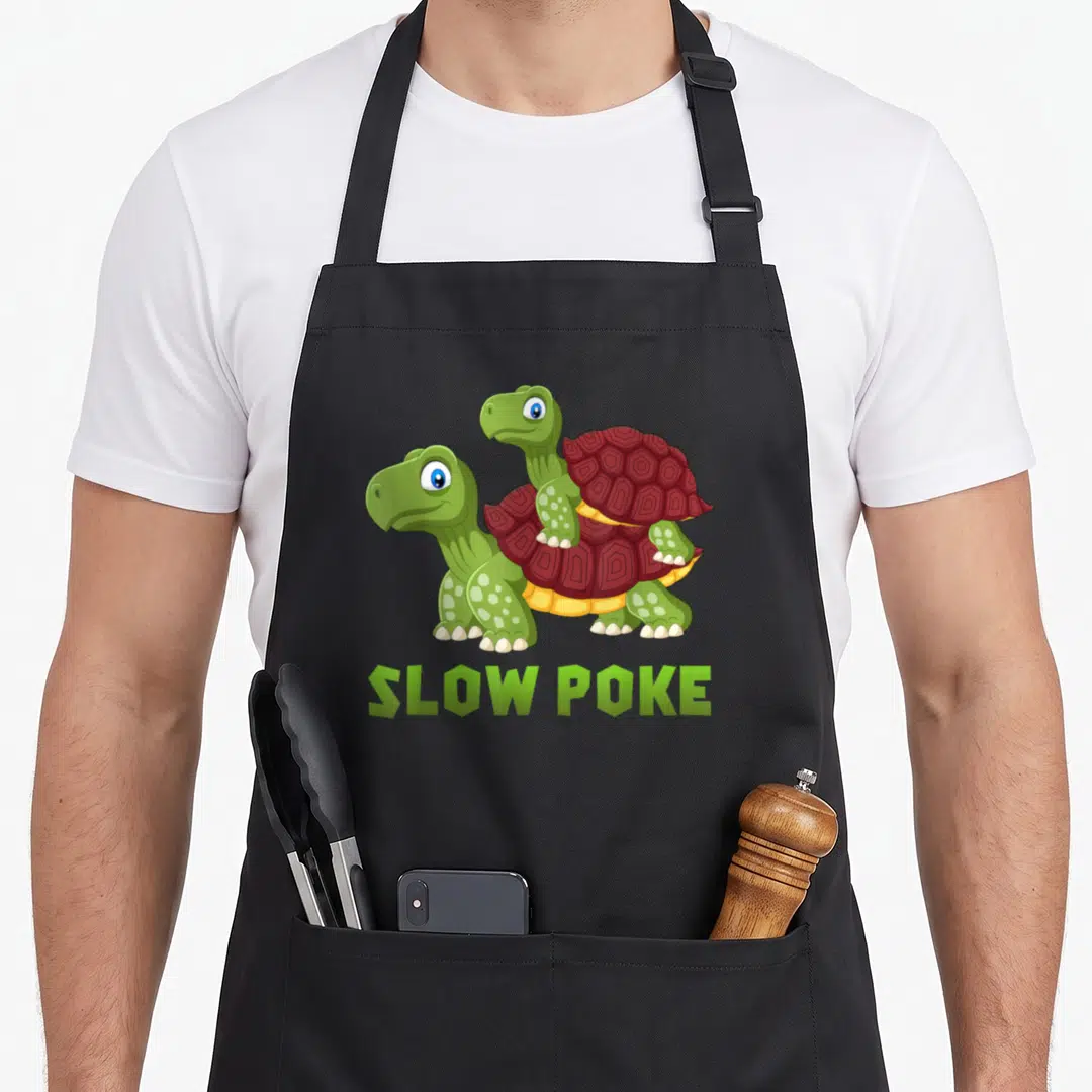 Slow dirty joke aprons - Two cartoon turtles stacked with green SLOW POKE text below — shown on a black cotton canvas apron against a white background