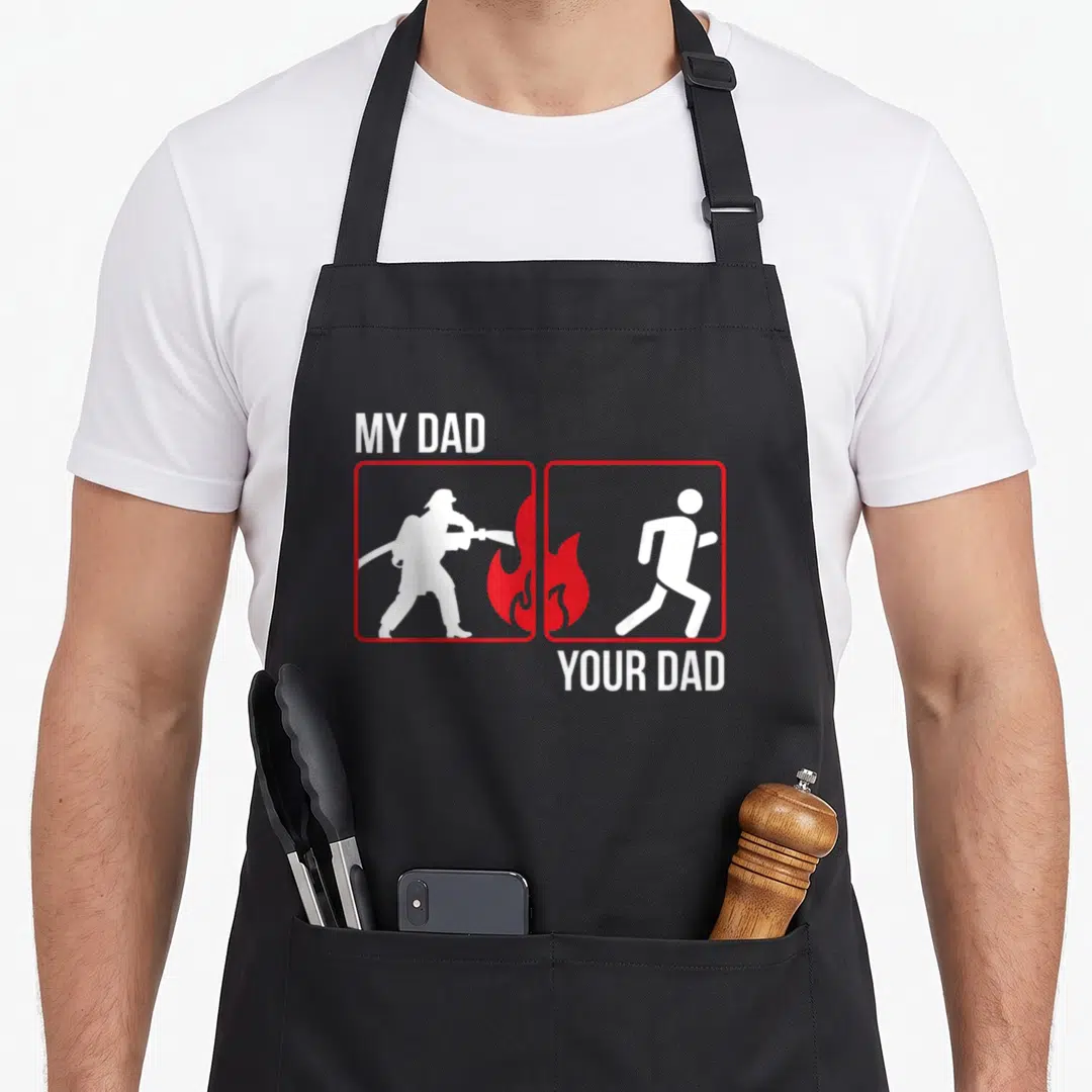 Son fireman firefighter aprons - My Dad Your Dad text with white firefighter and running person silhouettes in red — shown on a black cotton canvas apron against a white background