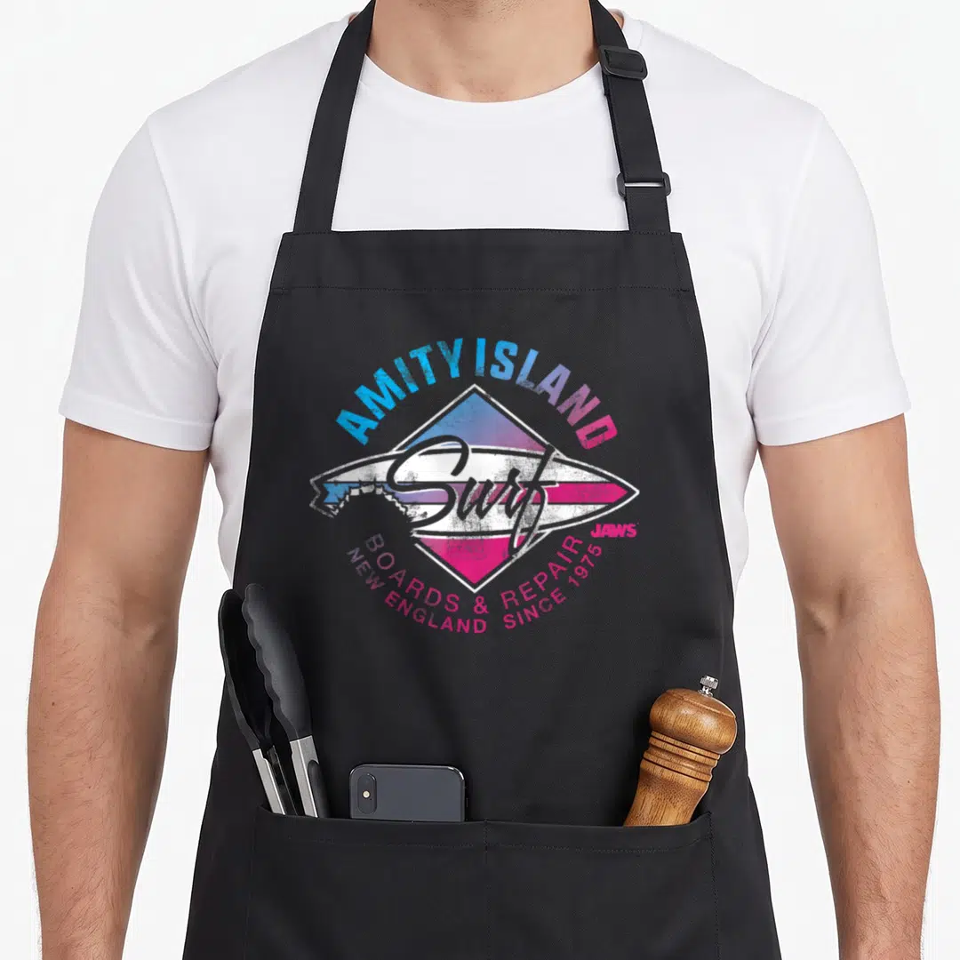 England kitchen island apron - Retro surfboard diamond logo with AMITY ISLAND Surf BOARDS & REPAIR text in blue and pink — shown on a black cotton canvas apron against a white background