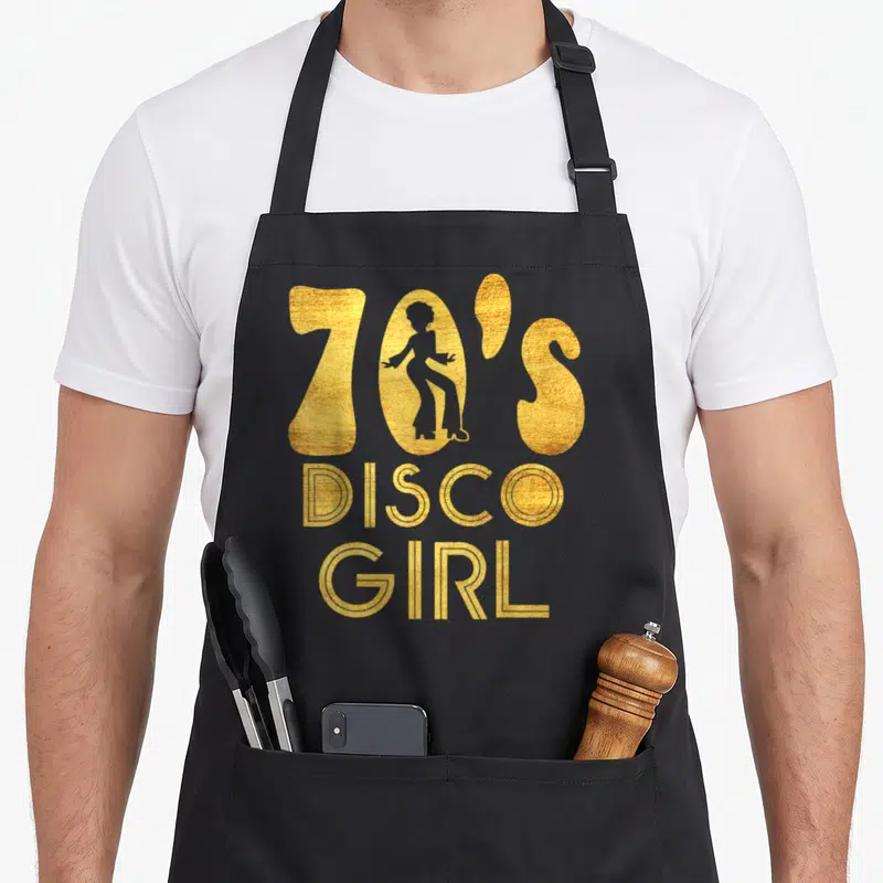 Seventy halloween apron - Gold 70'S DISCO GIRL text with woman silhouette in the zero letter — shown on a black cotton canvas apron against a white background