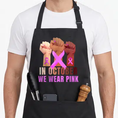 Fist breast cancer awareness aprons - Three raised fists in peach brown and dark brown tones behind pink ribbons — shown on a black cotton canvas apron against a white background