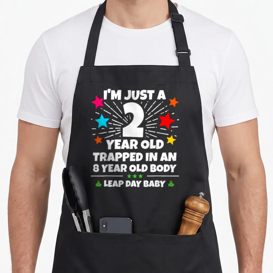 Leap 8th birthday apron - White 2 number with colorful stars and I'M JUST A 2 YEAR OLD TRAPPED IN AN 8 YEAR OLD BODY — shown on a black cotton canvas apron against a white background