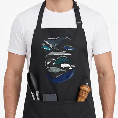 Breed whale apron - Nine labeled cartoon whales in dark blue, grey, and white with white text identifiers — shown on a black cotton canvas apron against a white background