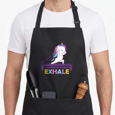 Sport training apron - Cartoon unicorn standing on purple reformer with multicolored EXHALE text below — shown on a black cotton canvas apron against a white background