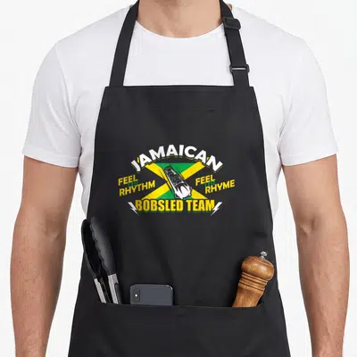 Jamaican buteo jamaicensis apron - Bobsled over yellow green X flag with Feel the Rhythm Feel the Rhyme text — shown on a black cotton canvas apron against a white background