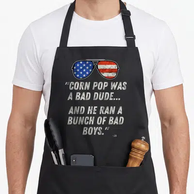 Pop dude apron - Sunglasses with US flag lenses above stacked quote text in distressed white font — shown on a black cotton canvas apron against a white background