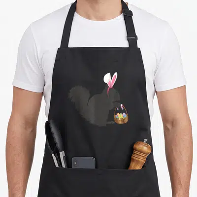 Squirrel basket apron - Black squirrel silhouette with pink bunny ears holding a brown basket of colorful eggs — shown on a black cotton canvas apron against a white background