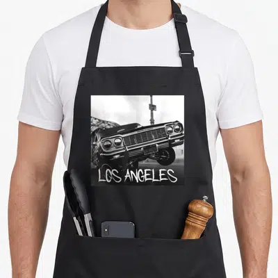 Los lowrider apron - Black and white photo of a classic car with LOS ANGELES text at the bottom — shown on a black cotton canvas apron against a white background