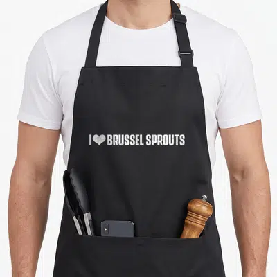 Brussel christmas apron - White distressed text I heart brussel sprouts on grey background — shown on a black cotton canvas apron against a white background