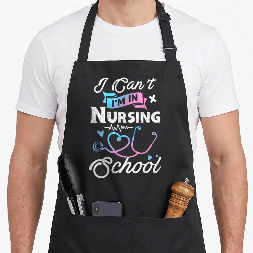 Funny school nursing apron - I Can't I'm In Nursing School text with gradient stethoscope heart and EKG line — shown on a black cotton canvas apron against a white background