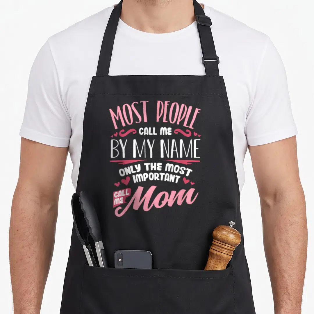 Cute mother's apron - Pink and white stacked text reading only the most important call me mom surrounded by heart — shown on a black cotton canvas apron against a white background