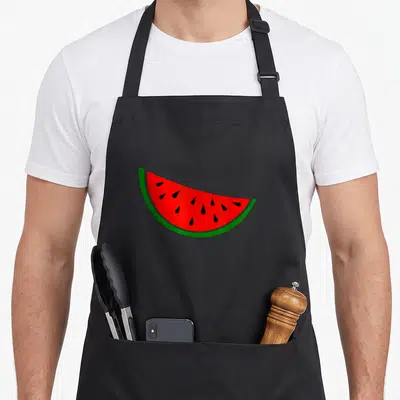 Funny watermelon apron - Cartoon watermelon slice with red flesh green rind and black seeds — shown on a black cotton canvas apron against a white background