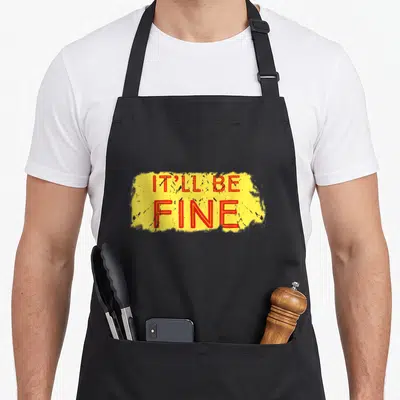 Relax snarky aprons - Red IT'LL BE FINE text on yellow paint splash background — shown on a black cotton canvas apron against a white background