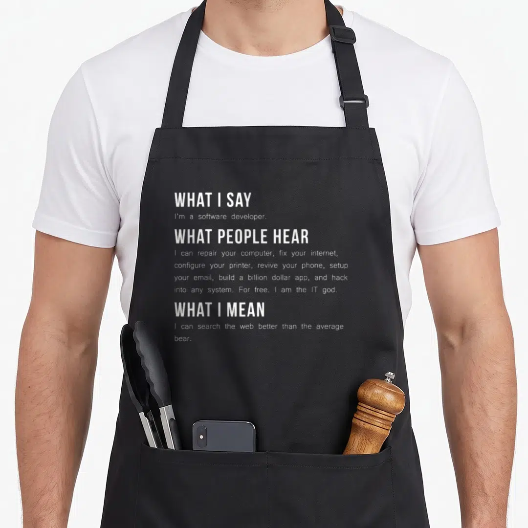 Programming software developer apron - White typography listing what people hear vs what a developer means about tech — shown on a black cotton canvas apron against a white background
