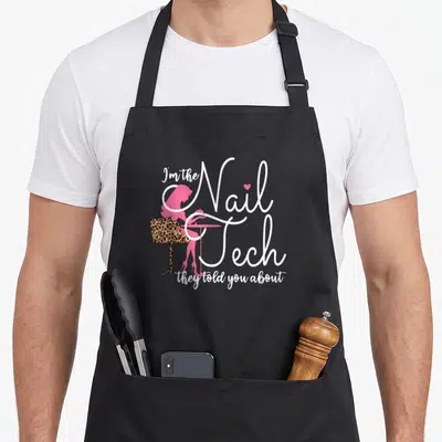 Pedicurist manicurist apron - Pink technician silhouette at leopard chair with Nail Tech text — shown on a black cotton canvas apron against a white background