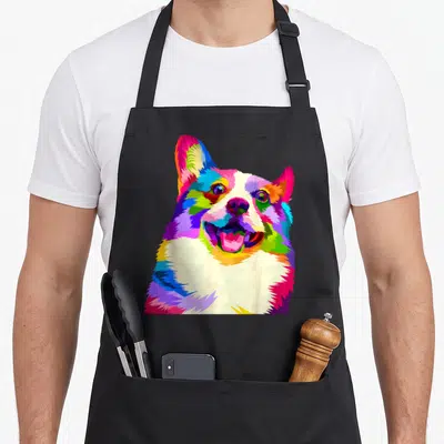 Pem welsh apron - Multicolored pop art corgi head portrait in blue red yellow green purple pink on black fabric — shown on a black cotton canvas apron against a white background