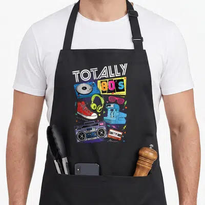 80s turntables and aprons - Cartoon 80s objects turntable headphones sneaker camera boombox cassette tape in blue pink — shown on a black cotton canvas apron against a white background