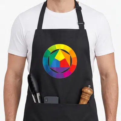 Wheel painter apron - Color wheel ring surrounding a five-section pentagon in yellow blue red green purple orange — shown on a black cotton canvas apron against a white background