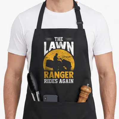 Landscaper rangers apron - Yellow sun with lawn tractor silhouette and distressed text THE LAWN RANGER RIDES AGAIN — shown on a black cotton canvas apron against a white background