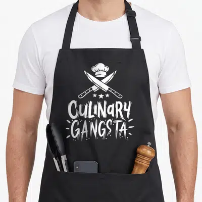 Cool culinary aprons - White chef hat over two crossed knives and three stars with CULINARY GANGSTA text — shown on a black cotton canvas apron against a white background