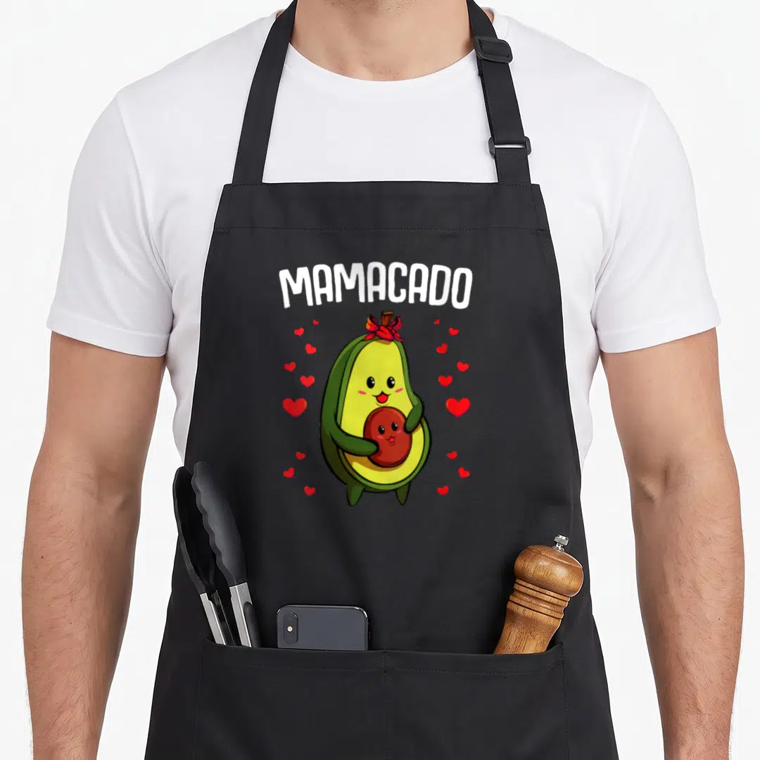 Pregnancy avocado apron - Cartoon avocado holding pit with red bow and hearts under MAMACADO text — shown on a black cotton canvas apron against a white background