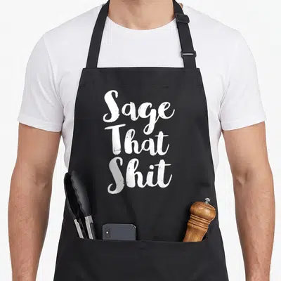 Cleaning sage apron - White stacked text reading Sage That Shit on grey background — shown on a black cotton canvas apron against a white background