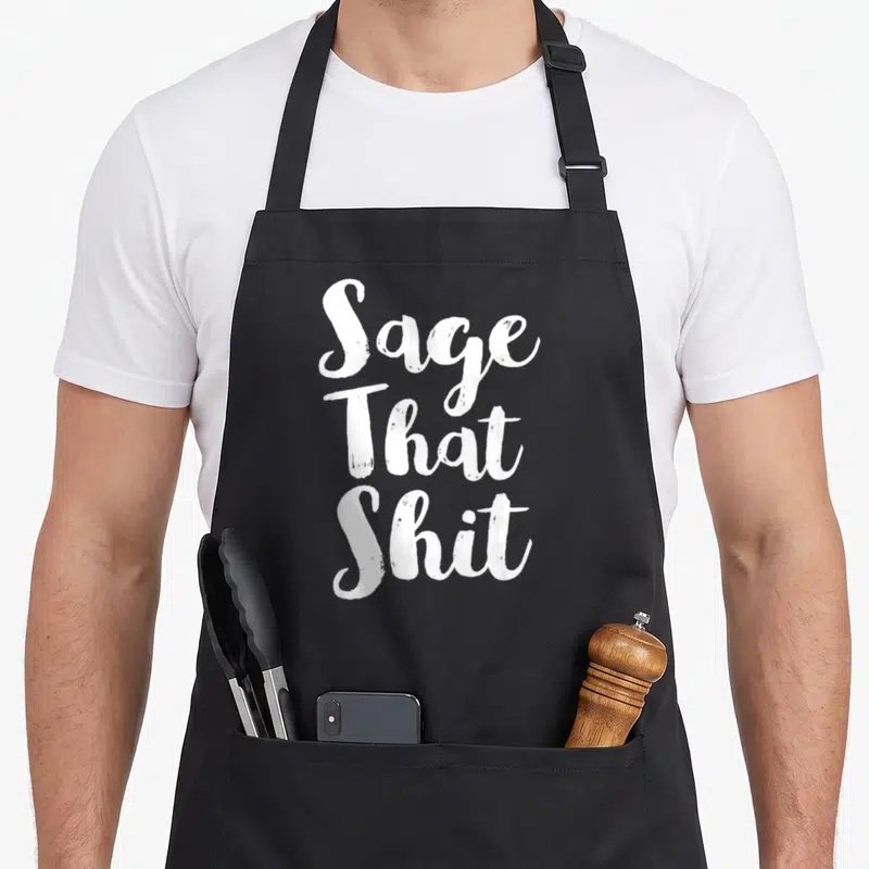 Cleaning sage apron - White stacked text reading Sage That Shit on grey background — shown on a black cotton canvas apron against a white background