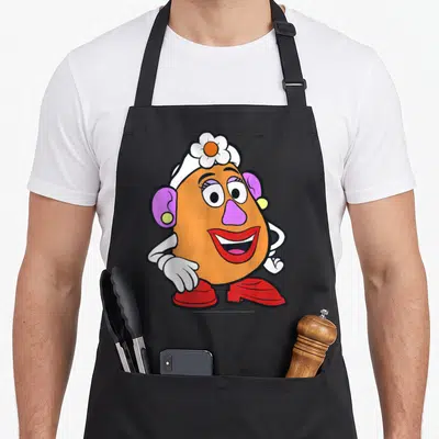 Potato mrs apron - Cartoon potato character with white hat, purple nose, and red shoes standing with hands on hips — shown on a black cotton canvas apron against a white background