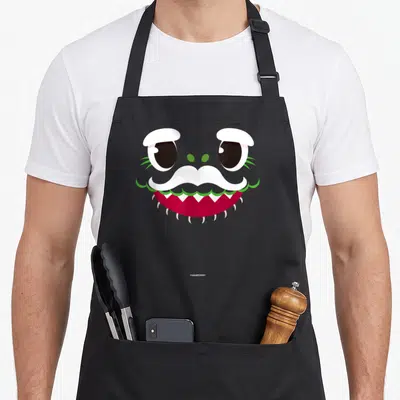 Baby grandpa apron - Cartoon monster face with white mustache, red mouth, green accents, and black eyes — shown on a black cotton canvas apron against a white background