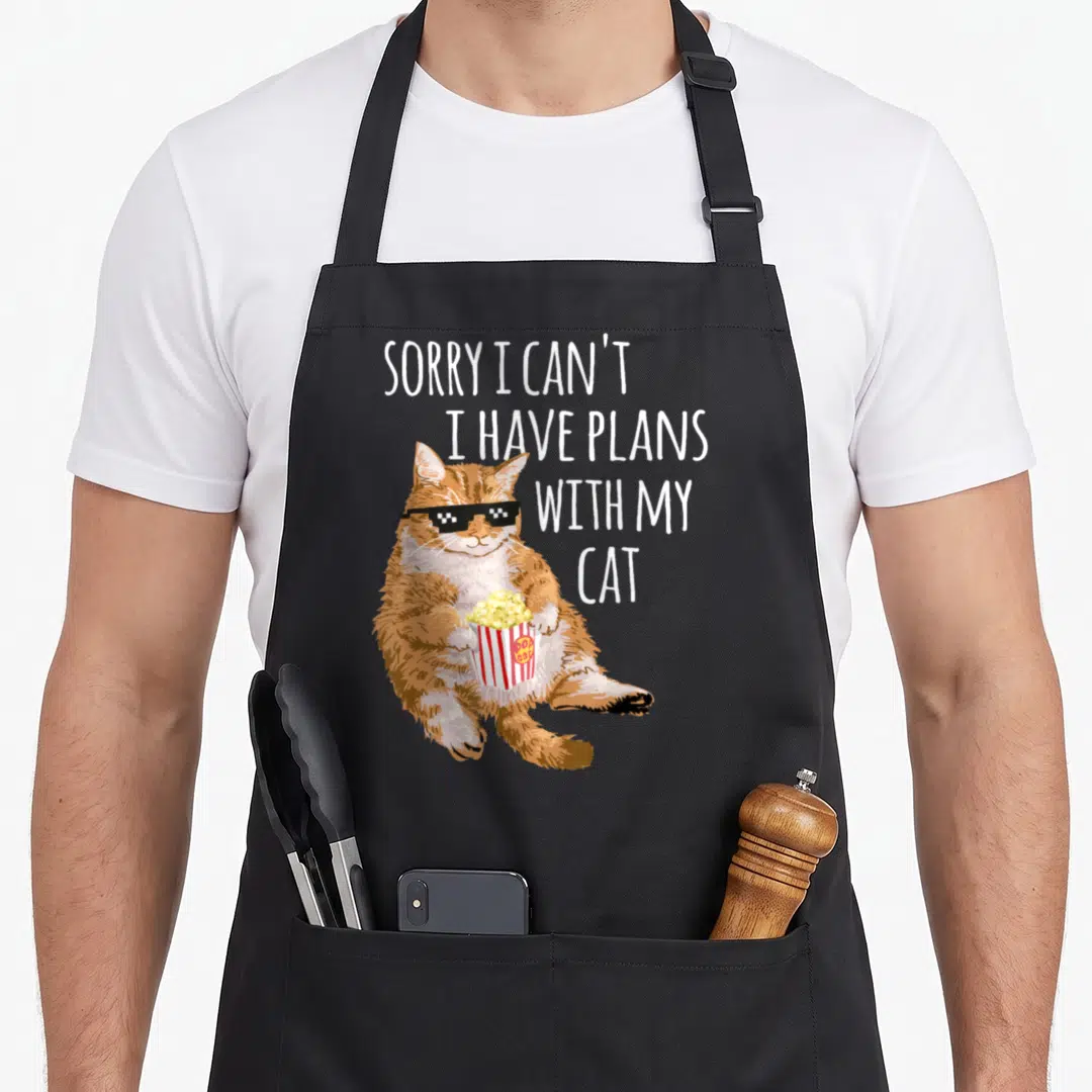 Sorry plan cat apron - Orange cartoon cat wearing pixel sunglasses holding popcorn bucket with stacked white text — shown on a black cotton canvas apron against a white background