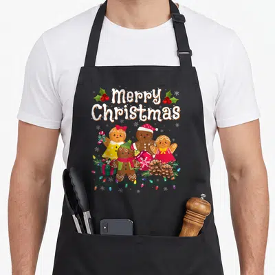 Merry women's christmas aprons - Four gingerbread people with gift, ornament, pine cones and string lights under Merry — shown on a black cotton canvas apron against a white background