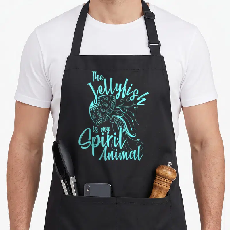 Funny jellyfish mom apron - Cyan line art jellyfish with text The Jellyfish is my Spirit Animal wrapping tentacles — shown on a black cotton canvas apron against a white background